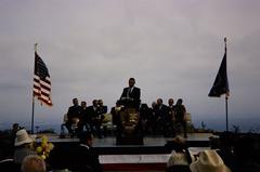 Man giving speech on a stage at Cabrillo National Monument with NPS arrowhead on microphone stand