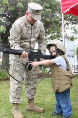 Gunnery Sgt. Brian Hahne helping a child hold a fake M-16A4 rifle during Bring Your Child to Work Day at Marine Corps Air Station Miramar