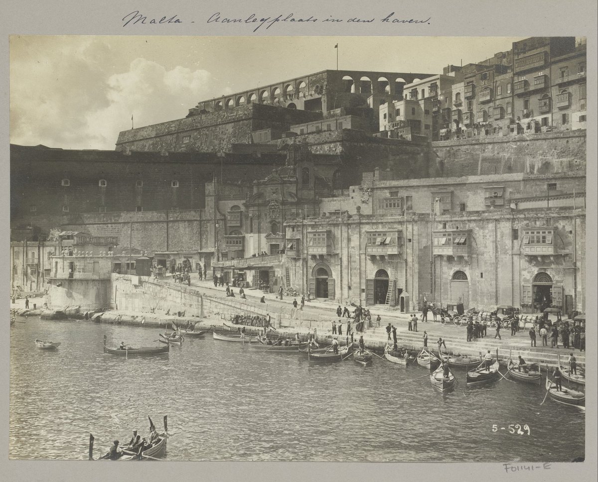 Early 20th-century black and white photo of a quay in Malta with ships and vehicles