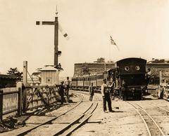 Standard gauge suburban train with 2-4-0T locomotive entering Cape Town station on dual gauge track with Castle of Good Hope in background