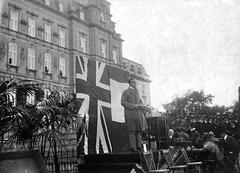 Minister Athanase David standing in front of the parliament building in Quebec during the unveiling of La Vérendrye statue with UK and French flags