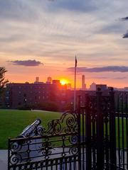 Sunset over Dorchester Heights gates with cannon and flagpole, Boston skyline in background