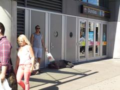 Pedestrians walking past a homeless man sleeping on the sidewalk at 10 Dundas Street East
