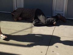 Pedestrians walking past a sleeping homeless man at 10 Dundas Street East urban sidewalk