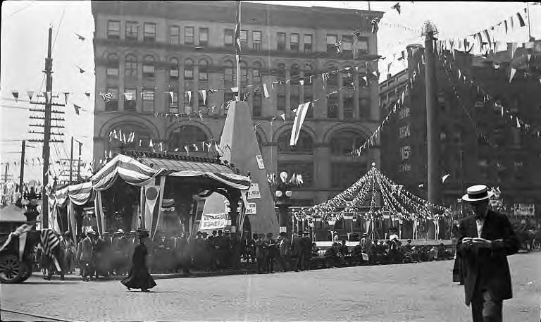 People and decorations in front of Mutual Life Building during Golden Potlatch event in Seattle 1912