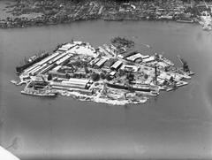 Aerial photograph of Cockatoo Island in Sydney Harbour with multiple naval ships docked, including HMAS Queenborough, HMAS Quiberon, HMAS Voyager, HMAS Bataan, Mortlake Bank, HMAS Koompartoo, HMAS Arunta, and the floating crane Titan, taken in 1951.
