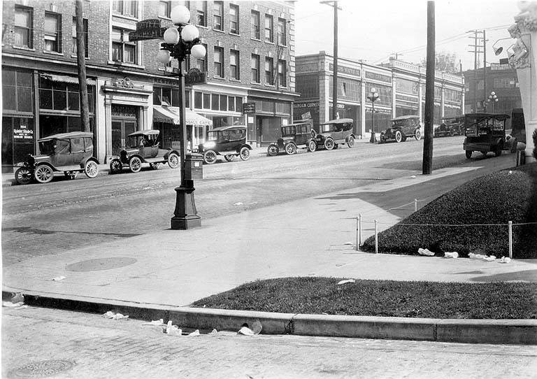 Vintage black and white photo of Pike Street near 10th Avenue in Seattle around 1920 showing cobblestone street with automobiles, trucks, street lights, apartment buildings, and businesses