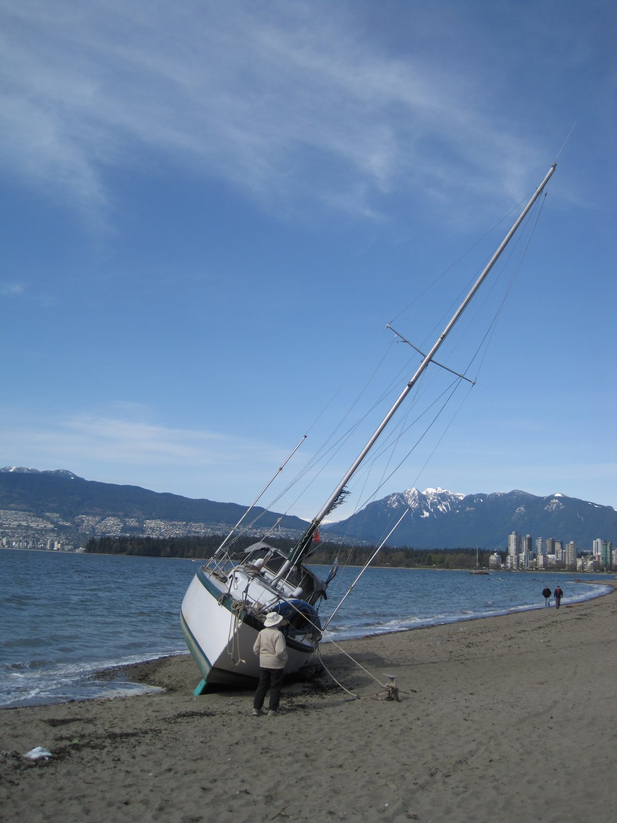 Beached damaged yacht on Kitsilano Beach in Vancouver after wind storm with Stanley Park and Downtown Vancouver in background