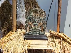 Gautama Buddha statue with chief disciples Moggallana and Sariputta surrounded by rice ears and straws at Bangkok Art and Culture Centre reflecting Buddhist and Thai folk beliefs