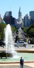 View down Benjamin Franklin Parkway from Philadelphia Museum of Art steps including museum fountain, The Washington Monument, Swann Memorial Fountain, and Philadelphia City Hall