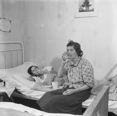 Two women eating and drinking, one lying on a bed in Bergen-Belsen repatriation camp in 1945
