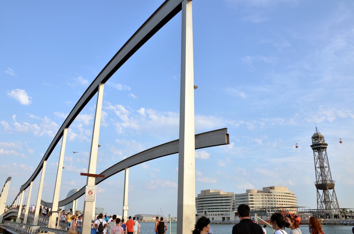 View of La Rambla de Mar wooden walkway and curved bridge over water in Barcelona