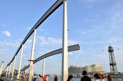 View of La Rambla de Mar wooden walkway and curved bridge over water in Barcelona