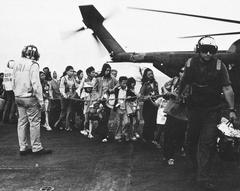Evacuees from Vietnam on flight deck of USS Midway during Operation Frequent Wind with USAF HH-53 Super Jolly Green Giant helicopter in background