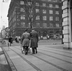 Two men pushing a baby stroller on a shopping street in Copenhagen, March 1954