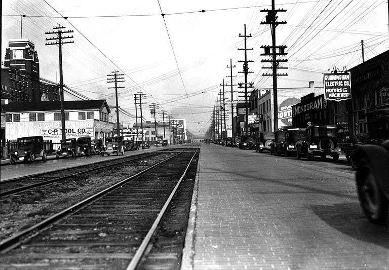 Historic street view of First Avenue South between South Lander Street and South Forest Street in Seattle on February 26, 1927, showing cobblestone streets, street railroad tracks, utility poles, and the Sears Tower on the left