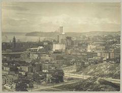 View of downtown Seattle from Beacon Hill in 1914 showing Chinatown, Smith Tower, Colman Dock, King Street Station, and dirt piles along unfinished Dearborn Street.