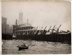 Ruins of Grand Trunk Pacific Dock after fire in Seattle, 1914, viewed from rowboat with Smith Tower in background