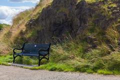 Wooden bench on grassy area at Calton Hill with scenic view of Edinburgh city and hills