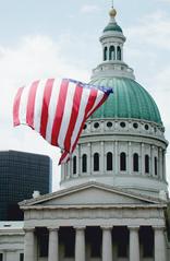Dome of the Old Courthouse in St. Louis with large American flag flying in the foreground against urban backdrop