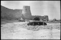 Wall of Qatif Castle with one of its towers and piles of limestone stones for gypsum and painting works taken in 1930