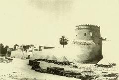 View of Qatif Castle wall with one of its towers and piles of limestone stones in front, used for plaster and paint work, 1930