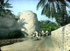 Part of Qatif Castle tower and wall with locals and donkeys heading towards farms