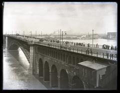 Black and white photo of Eads Bridge over Mississippi River during high water in 1903 with pedestrians, streetcar, and carriage