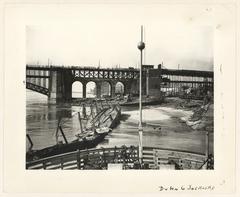 Black and white photo of Eads Bridge east end showing tornado damage with debris and wrecked boats along shore in May 1896