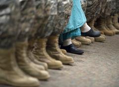 Nurse in blue scrubs among soldiers in camouflage pants and tan combat boots listening to Army Chief of Staff's address