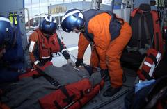 U.S. Coast Guard Petty Officers transferring injured fisherman from HH-60 Jayhawk helicopter cabin during medical evacuation
