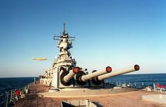 Close-up view of Mark 7 16-inch 50-caliber guns on the battleship USS Wisconsin during Operation Desert Storm with a British BAe Nimrod aircraft flying overhead