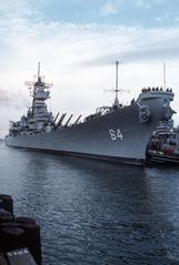 Crewmen manning the rails as harbor tug Marinete maneuvers battleship USS Wisconsin into port at Naval Air Station Norfolk Virginia