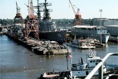 Battleship USS Wisconsin departing pier with sailors and shipyard workers watching, destroyer USS John Hancock tied up at center in Pascagoula, MS, December 1 1989