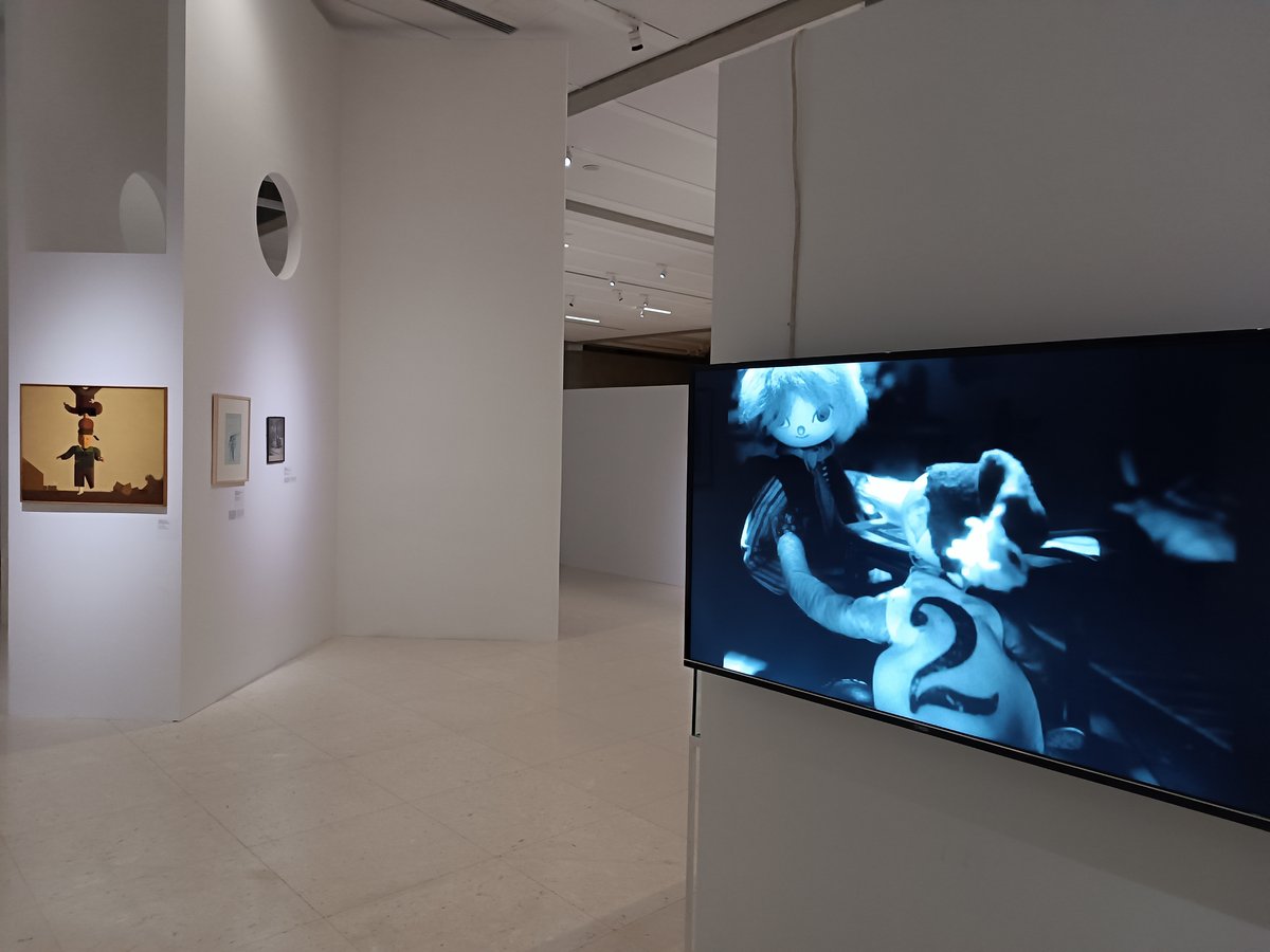 Surrealist cartoon from Aktivitet: 100 godina nadrealizma exhibition with Milenko Stančić's painting Sunday Walk in the background
