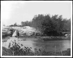 Man standing near a water ditch at the bank of Los Angeles River, north side of Griffith Park, circa 1900