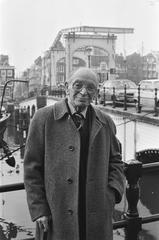 Sylvain Poons, elderly Dutch stage actor, cabaret artist and director, standing by Magere Brug in Amsterdam