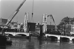 Damaged bridge section being lifted onto a barge in Amsterdam with cranes and ships in the background