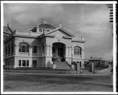 Exterior view of the Charles M. Stimson Library building on Occidental College Highland Park campus around 1908, showcasing Beaux-Arts architectural style with extended porch, pediment with building name, multifoil tracery windows, turret-like tower, and stone masonry wall.