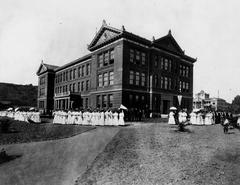 Group of formally-dressed graduates posing by the historic Hall of Letters building at Occidental College in 1904