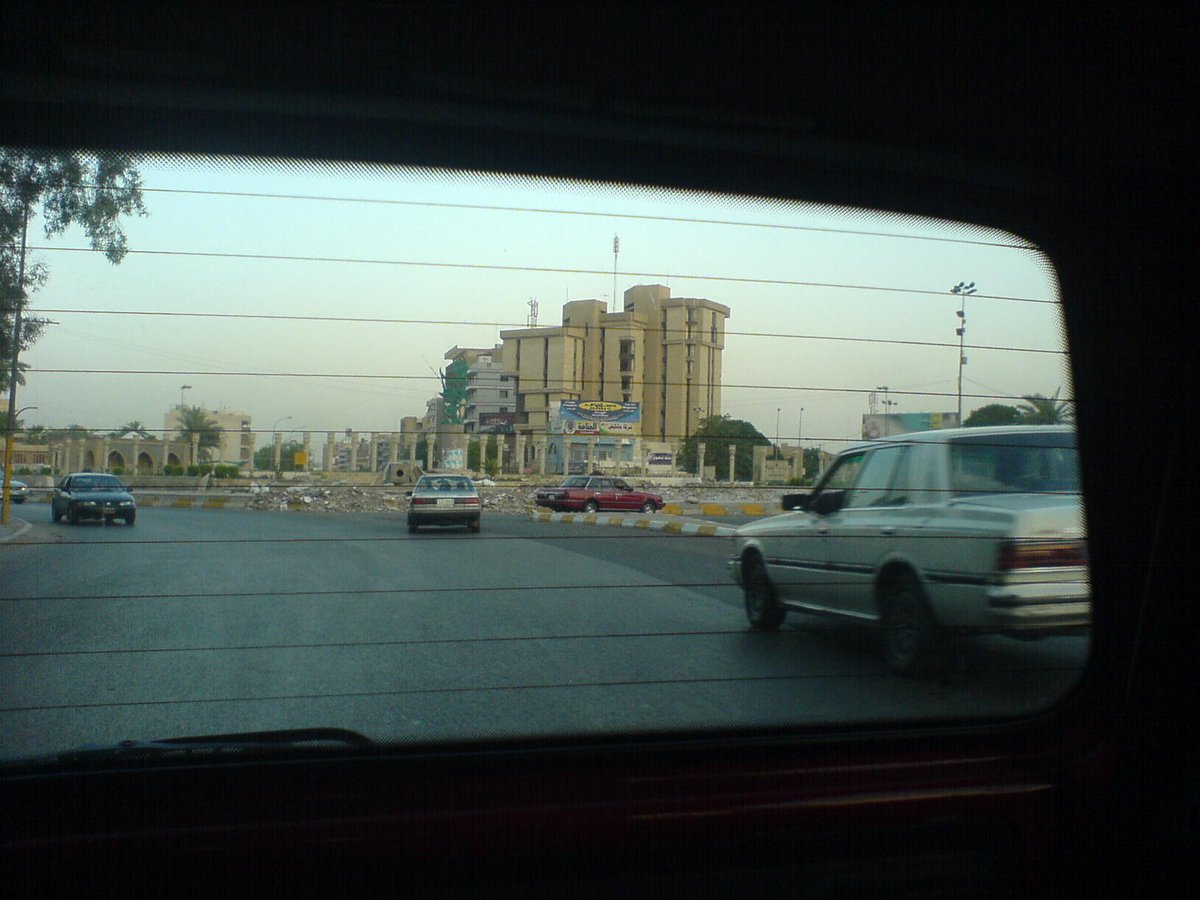Firdos Square in 2006 with a crowd assembling around the toppled statue in a sandy urban area