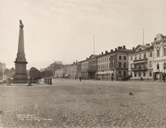 Empty Kauppatori market square with horse carriages behind Empress Stone, Northern Esplanade building row, people walking and cycling, light cloudy sky, doves on the square, 1890