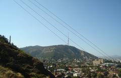 Panoramic view of Mt. Mtatsminda and downtown Tbilisi with city buildings and green hills under a clear blue sky