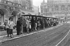 Crowd waiting at a busy tram stop on Leidseplein in Amsterdam during persistent frost and snowy winter weather