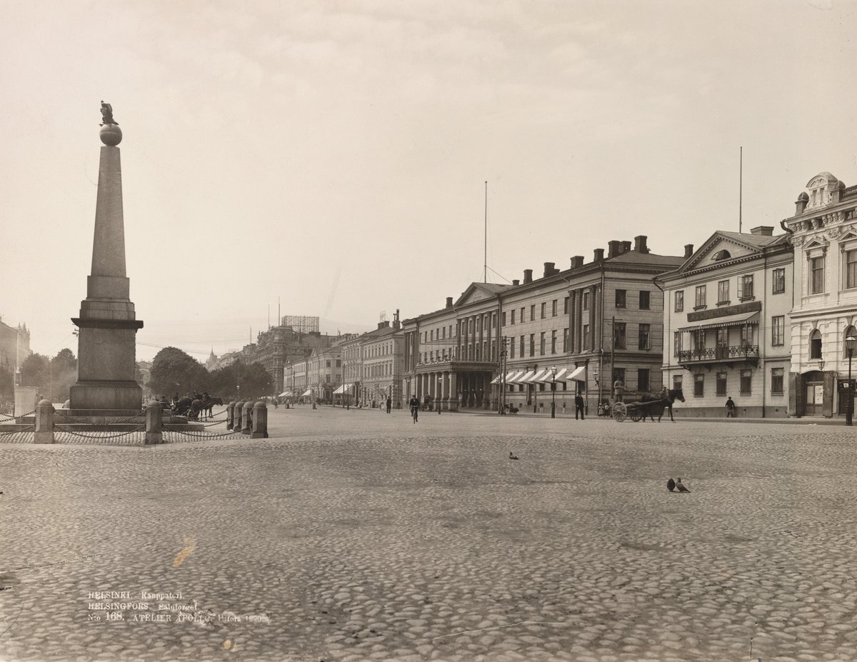 Historic empty market square with horse-drawn carriages behind the Empress's stone and people walking and cycling on a North Esplanadi street under a partly cloudy sky