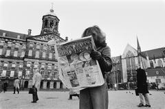 Girl reading morning newspaper with large headline about Queen Juliana's abdication on the Dam square, Amsterdam with Royal Palace on the left and Nieuwe Kerk on the right