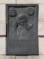 Memorial plaque honoring Pope John Paul II on the facade near the main entrance of the Holy Cross Basilica in Warsaw