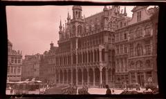 Brussels City Museum with parked automobiles and wagons in Grand Square, flower market stalls with umbrellas visible