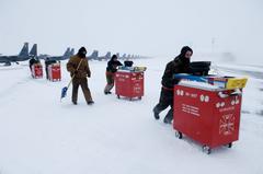 U.S. Air Force airmen pushing tool chests through snow on flight line at Elmendorf Air Force Base