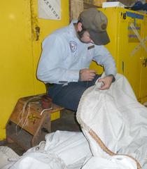 Volunteer sewing leather chafe gear onto a canvas mizzen staysail
